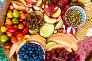 colorful array of healthy foods on a tabletop; fruits, nuts, tomatoes, and crackers