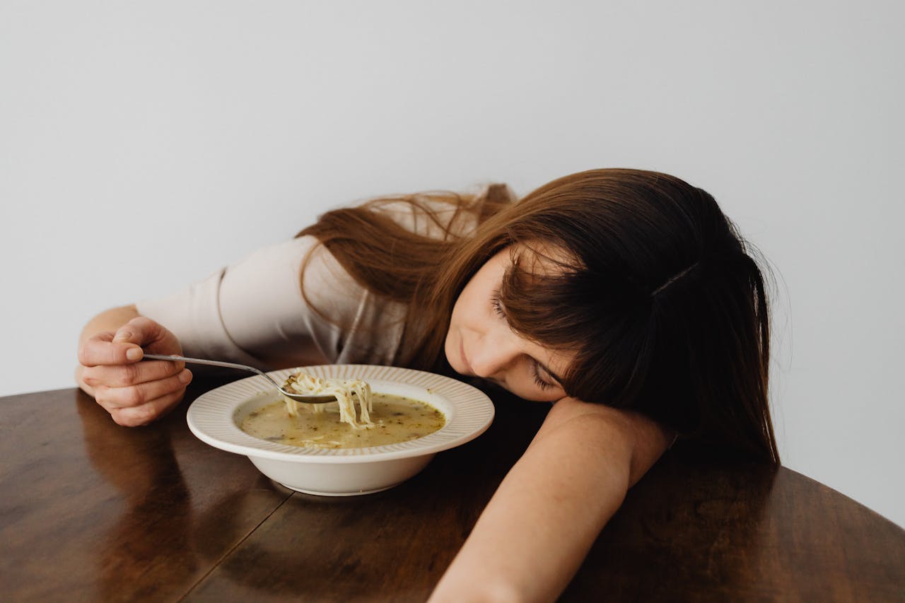 Tired woman falling asleep while eating soup, showing fatigue and low energy after a meal